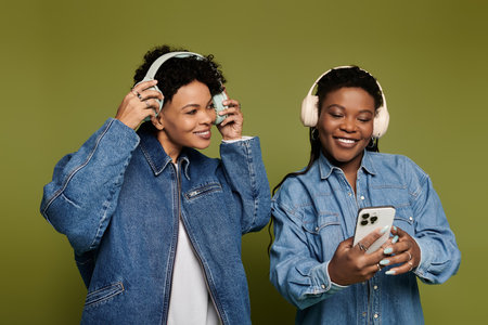 Two fashionable women share a joyful moment listening to music while wearing trendy outfits.のeditorial素材