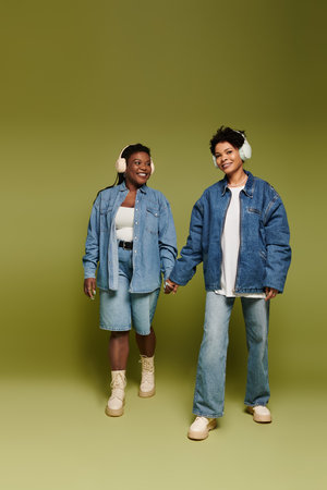 Two fashionable women enjoy each others company while wearing trendy attire and headphones.の写真素材