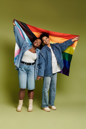 Two fashionable women warmly hold a rainbow flag, expressing love and unity in a striking setting.の写真素材