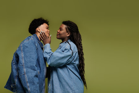 Two stylish women share a loving kiss, radiating joy and fashion against a vivid green background.の写真素材