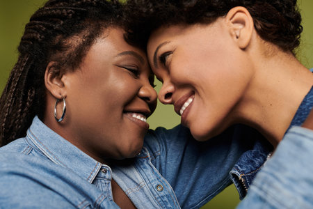 Two stylish women joyfully embrace in front of a vibrant backdrop.