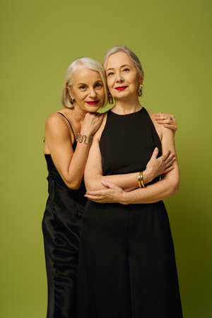 Two fashionable mature women embrace each other joyfully against a lively green backdrop.