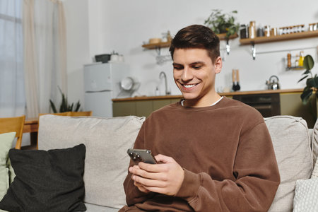 A young man smiles on his couch, enjoying his smartphone and the cozy atmosphere.の写真素材