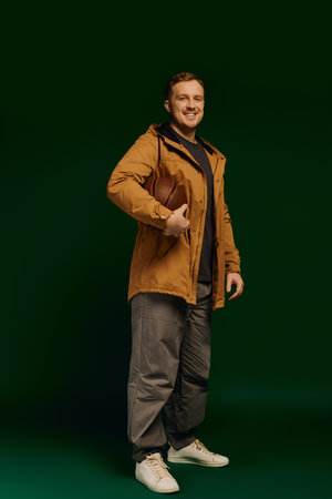 A confident man in casual clothes stands in a studio, wearing a charming smile.