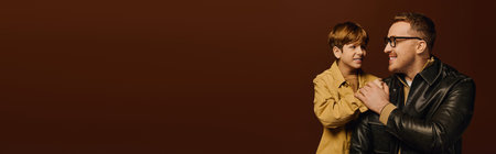 Father and son enjoy a fun moment in a studio, dressed in trendy, casual outfits and smiling, banner