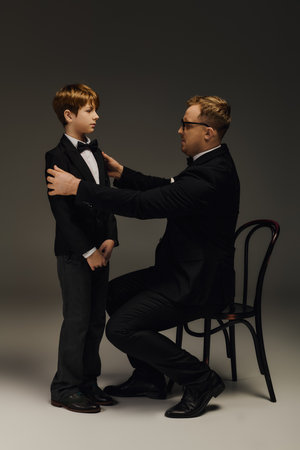 Father adjusts the bow tie of his son in an elegant studio atmosphere, showcasing family love.の写真素材