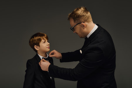 A handsome father adjusts the bow tie of his son, both elegantly dressed for a special occasion.の写真素材