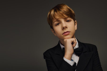 A stylish preteen boy poses thoughtfully in elegant attire featuring a classic bow tie.の写真素材