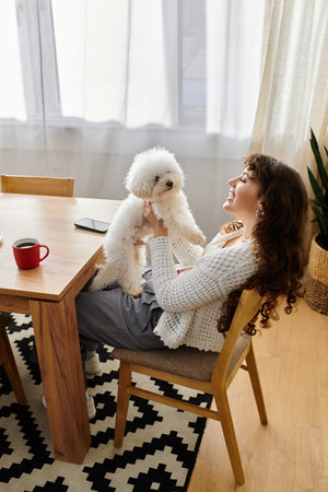A young woman shares a playful moment with her fluffy dog at a bright wooden table.のeditorial素材