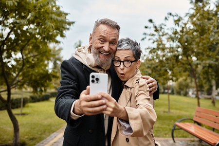A mature couple smiling and posing together while taking a selfie in a lovely park.