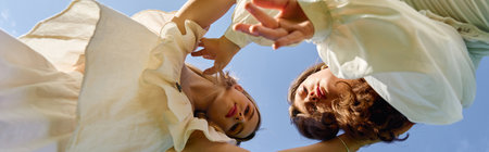 Two fashionable women express their confidence under a brilliant blue sky surrounded by nature.