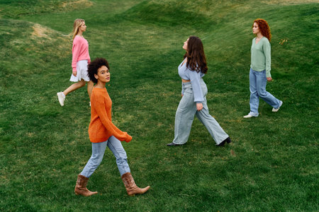 Stylish women stroll in a green park, displaying their unique fashion under clear skies.の写真素材