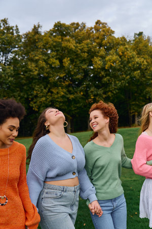 Four fashionable friends walk hand in hand, radiating confidence in the vibrant spring park.