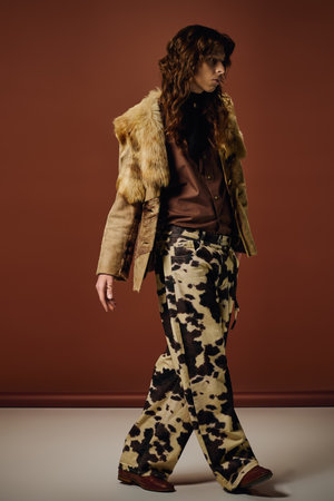 A fashionable young man strides confidently in a striking outfit against a warm backdrop.