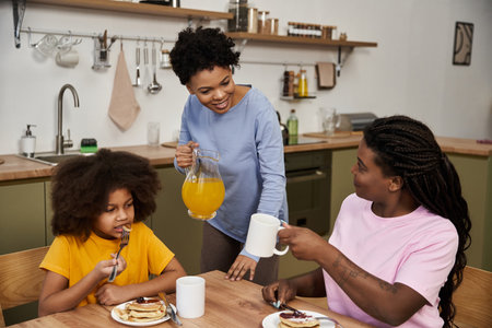 Family bonding over pancakes and juice in a warm kitchen, celebrating love and connection.の写真素材