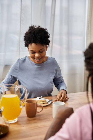 A joyful family shares breakfast, savoring pancakes and drinks while bonding in a warm atmosphere.の写真素材