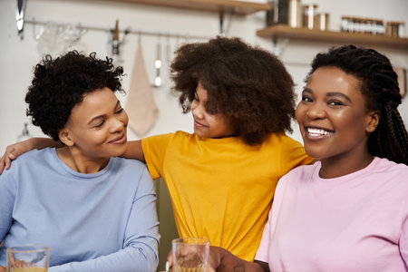 A young daughter smiles between two mothers, sharing joy during family bonding time at home.の写真素材