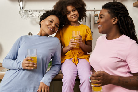 A joyful family shares laughter and bonding over refreshing drinks in a warm kitchen space.の写真素材