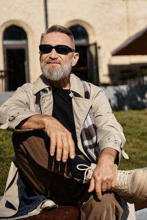 Stylish senior man enjoying a sunny day in the city, exuding confidence and charm while seated outdoorsの写真素材