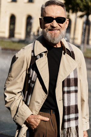Stylish senior man with a trendy scarf walks confidently in a vibrant urban setting during a sunny afternoonの写真素材