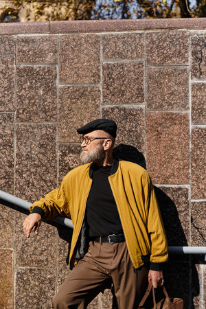 Stylish senior man with a dapper look enjoys a leisurely moment in the urban cityscape during a sunny afternoonの写真素材