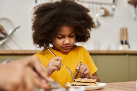 Loving family gathers in a warm kitchen as their daughter indulges in delicious pancakes.の写真素材