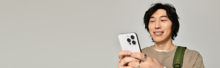 Handsome young asian male enjoys his time engaging with his smartphone in a stylish pose.のeditorial素材