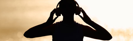 A beautiful athletic woman stands on the beach, listening to music while the sun sets behind her.の写真素材