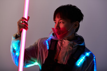 Young and handsome Asian man showcases a modern style with neon elements at twilight.の写真素材