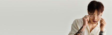 A fashionable young Asian man adjusts his glasses while sporting casual, contemporary attire.の写真素材