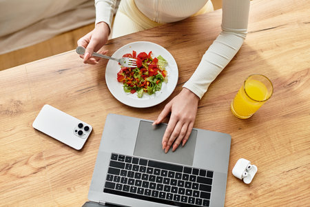 view from above of young woman enjoys a nutritious salad with a glass of juice while using her laptop.の写真素材