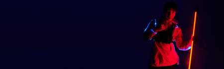 Young Asian man stands confidently with vibrant lights, showcasing his stylish outfit.の写真素材