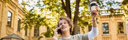 Stylish student joyfully talks on the phone with a drink in hand amidst a vibrant campus setting.のeditorial素材
