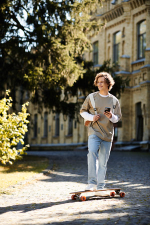 A young man skates down a sunny path, smiling and checking his phone.