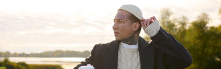 Handsome man with tattoos showcases his trendy outfit while sipping coffee in natures beauty.