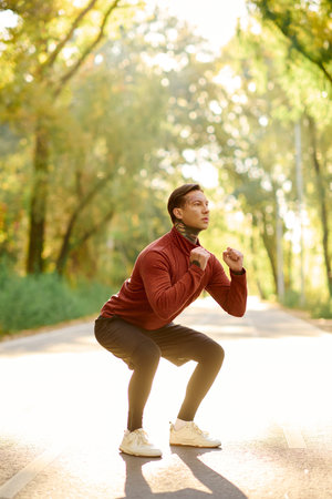 Tattooed man does stylish squats on a peaceful nature path.