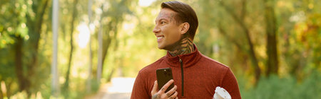 Handsome man with tattoos smiles as he walks through a sunlit path, enjoying the moment.