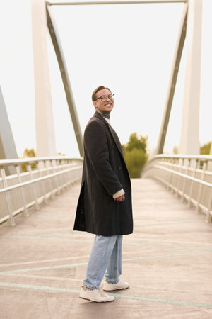 A confident young man showcases his trendy style while standing on a sleek bridge at sunset.のeditorial素材