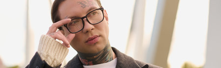 Handsome man with stylish attire and tattoos poses confidently, showcasing urban fashion sense.
