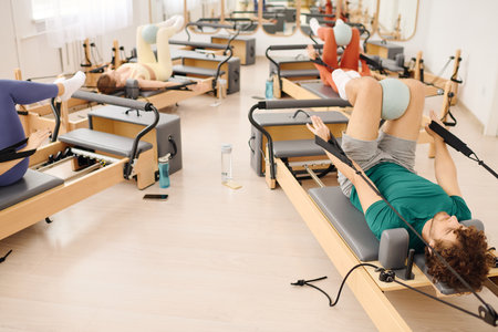 Participants engage in a focused pilates class utilizing reformer equipment to enhance strength.の写真素材