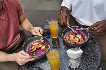 Two men share a joyful moment at a cafe, savoring colorful meals and drinks together.の写真素材