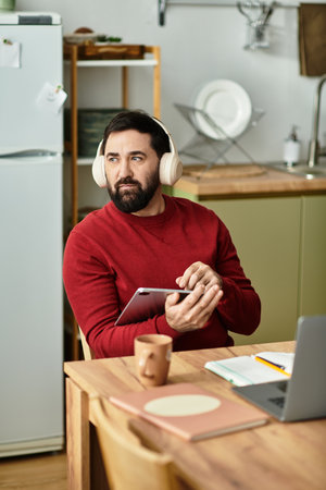 A stylish senior man in casual wear enjoys music with headphones while holding a tablet.のeditorial素材