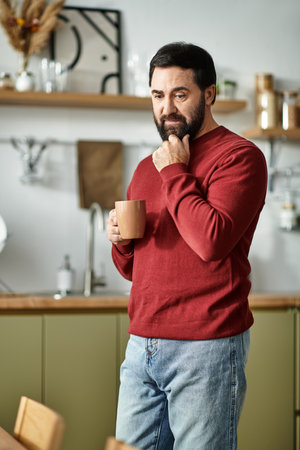 Elderly man in casual attire thoughtfully enjoying his warm beverage in a cozy kitchen setting.の写真素材