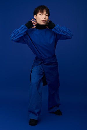 Striking young asian man stands confidently in bold blue attire, exuding charm and style.のeditorial素材
