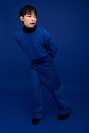 A stylish young man stands playfully, surrounded by rich blue tones, showcasing his charm.のeditorial素材