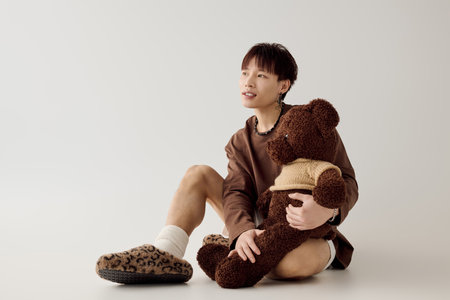 Young man sits comfortably with a teddy bear, exuding charm and warmth in a serene space.の写真素材