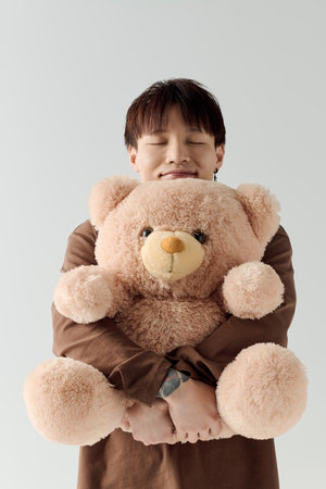A young man smiles while hugging a large, fluffy teddy bear, exuding warmth and joy.のeditorial素材