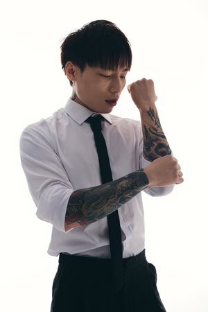 A stylish young Asian man adjusts his dress shirt, showing off intricate tattoos in a bright space.のeditorial素材