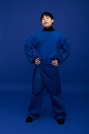 Confident young Asian man poses with hands on hips, flaunting his striking blue outfit.のeditorial素材