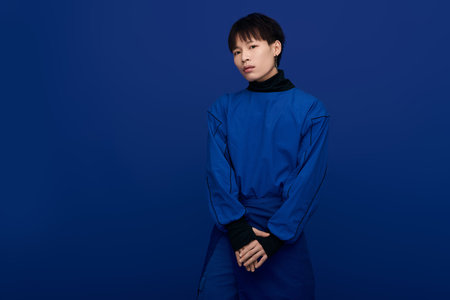 A handsome Asian man stands confidently against a vibrant blue background, exuding charm.